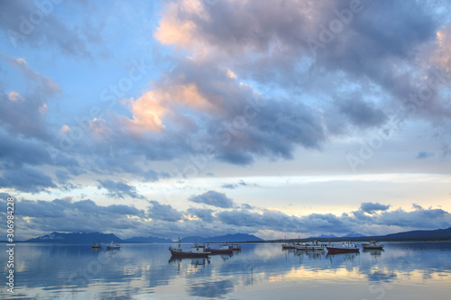 fishing boats are reflected in the sea in a quiet bay in a cloudy sunset in Patagonia