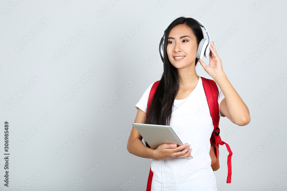 Beautiful young woman holding tablet pc and headphones on grey background Beautiful young woman holding tablet pc and headphones on grey background