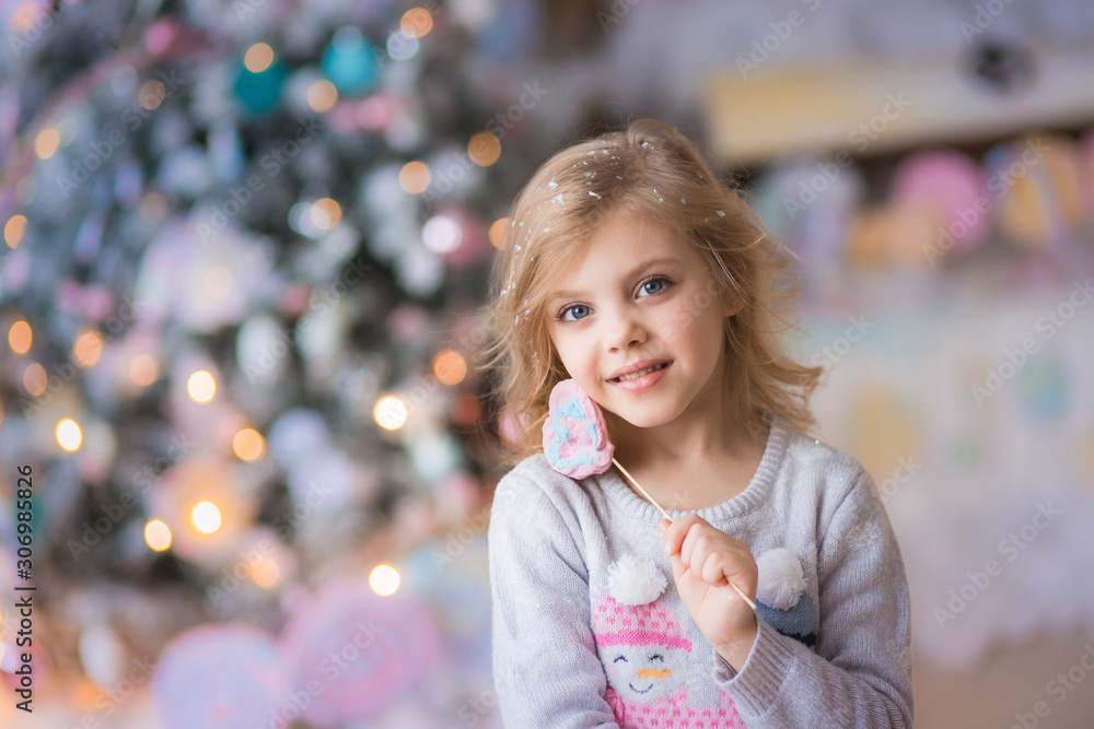Portrait of a fair-haired beautiful curly happy smiling girl 6-7 years old in the New Year's Eve on Christmas Eve against a background of lights, smiling with lollipops in her hands