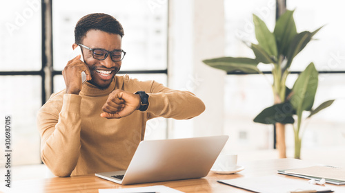 Happy black guy looking at watch talking on phone photo