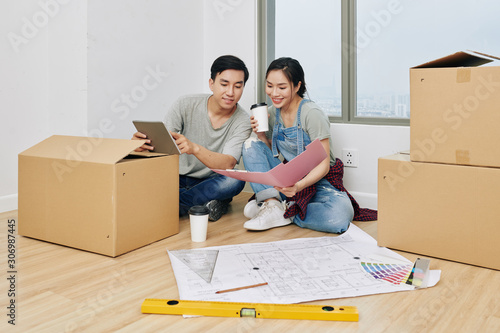 Fotografi Cheerful young Vietnamese couple discussing construction plans in documents and