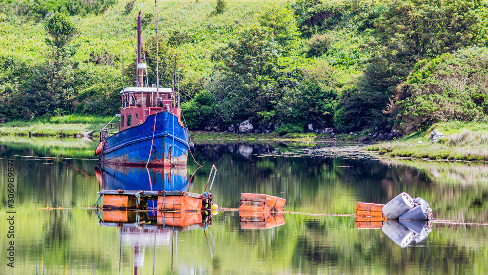 Fishing boat anchored in the middle of Clifden Bay at high tide, with buoys floating, beautiful reflection in the water on a sunny spring day in Clifden, Ireland