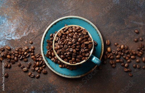 Natural organic roasted coffee beans in blue cup on dark rusty background.