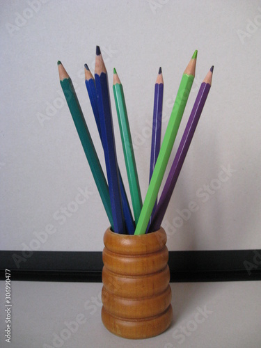 lápices de colores en gamas de verdes, azules y morados en porta lápices marrón con fondo de carpeta gris y negro. Lápices para dibujar y hacer bocetos. photo