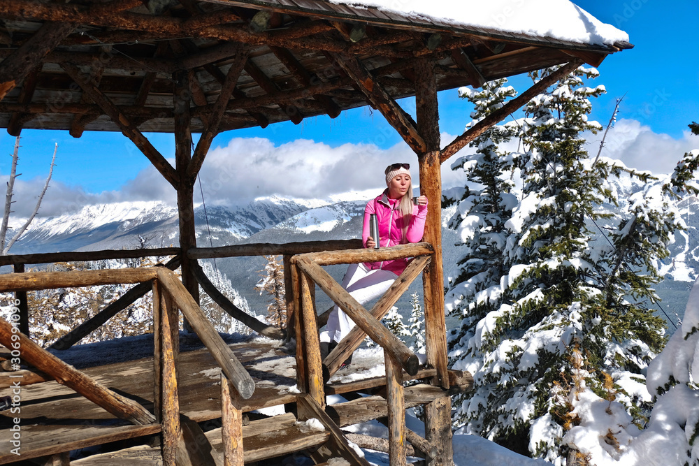 Young blond woman skier drinking tea on mountain top veranda.  Winter in Canadian Rockies. Lake Louise ski resort. Alberta. Canada