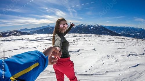 A girl holding a man's hand on a snowy background in Bad Kleinkirchheim, Austria. Follow me to winter wonderland! She is happy, having fun. There is a lot of snow caped mountain in the back.