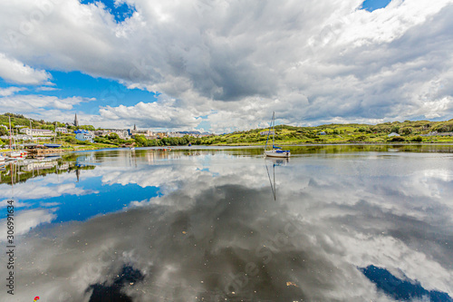 Clifden harbor at high tide  boats anchored with clouds reflecting in the water and the village in the background  sunny spring day with a blue sky and abundant white clouds in Clifden  Ireland