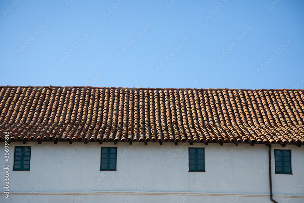 Red tile roof on a stucco building, with a blue sky background Red tile roof on a stucco building, with a blue sky background