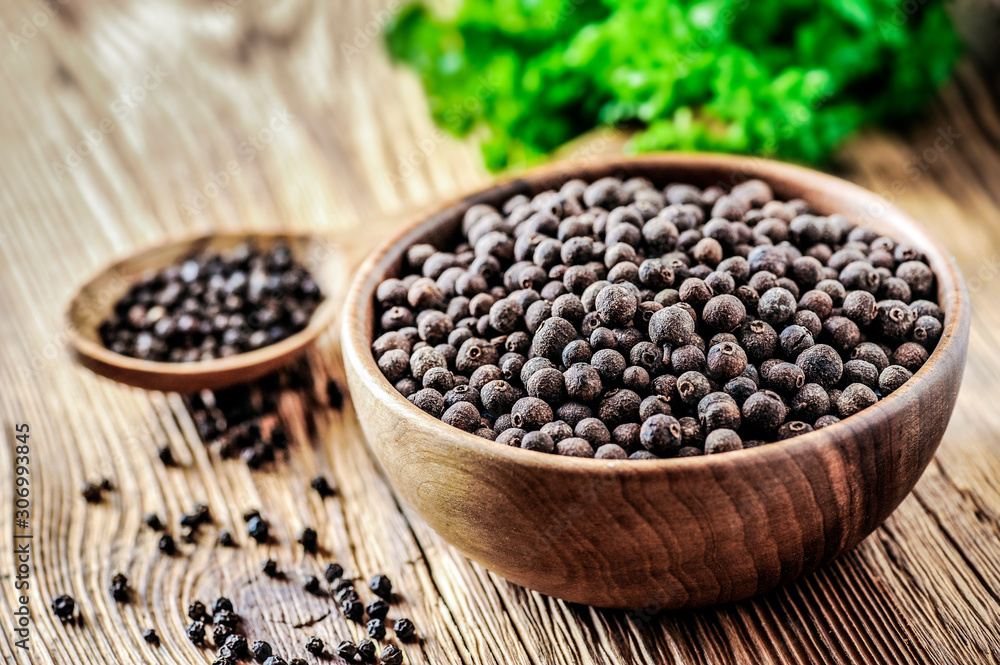 Black pepper. Black dry pepper in wooden bowl on wood table with green background. Black pepper. Black dry pepper in wooden bowl on wood table with green background.