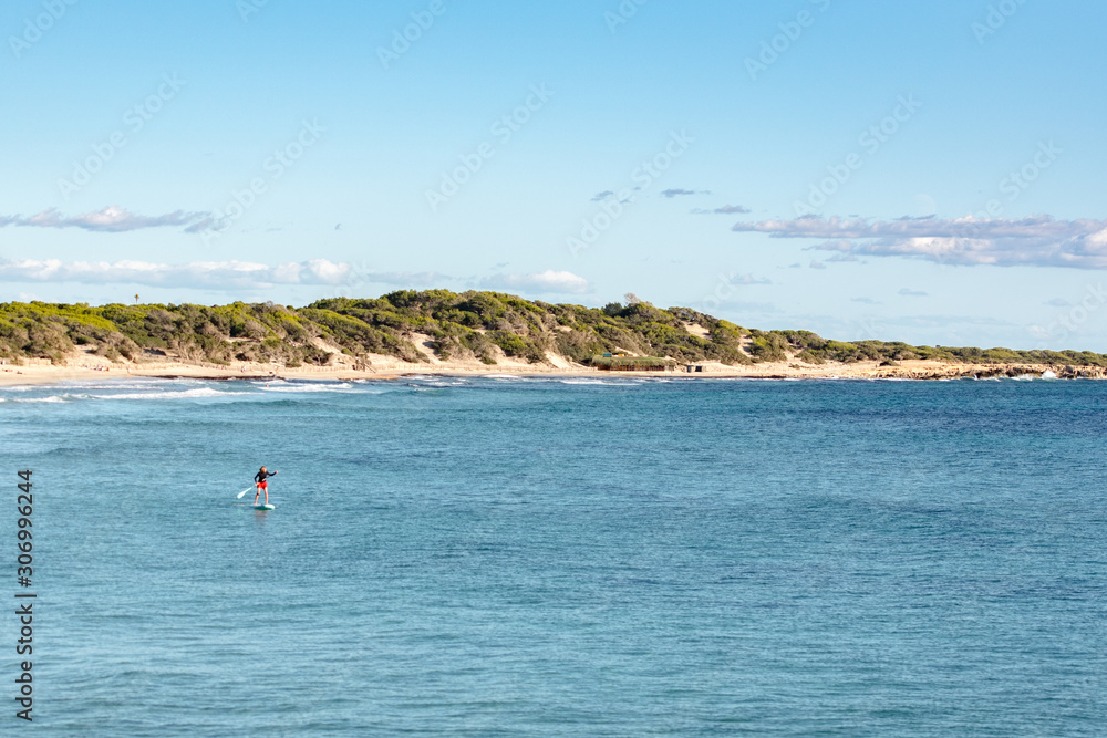 Man practicing paddle surfing through the deserted beaches of Ses Salines in the Ses Salinas National Park of Ibiza and Formentera, Spain.