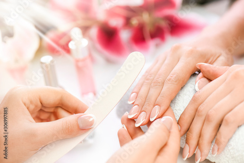 Woman beautician using  a nail file. Professional and beautiful hands with nails care manicure applying in luxury salon. Pink red flowers background.