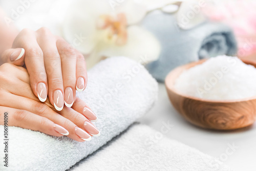 Luxury nails french manicure concept. Woman in cosmetics salon with towels, salt in olive bowl and flowers in background. Relaxing hands massage or spa treatment procedure.