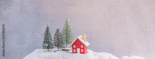 Miniature wooden red house on the snow over blurred Christmas decoration background, toned, snowflakes effect