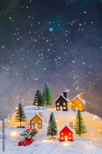 Miniature wooden houses village on the snow at night over blurred Christmas starry decoration background, toned
