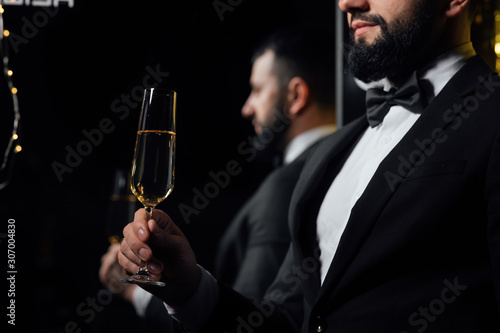 Successful handsome man in classic suit holds a glass of champagne. Bearded man in classic suit having luxury style. Merry Christmas and a happy new year 2020. Reflected in the mirror