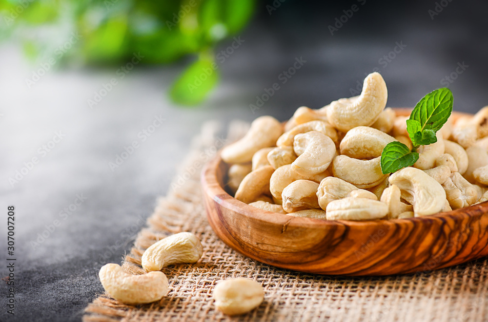 Fresh Cashew nuts in white wooden bowl on black stone table. Delicacies nut on dark background.