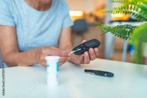 Woman checking blood sugar level while sitting at home. Woman using lancelet on finger. Diabetes checking blood sugar level. Woman using lancelet and glucometer at home.
