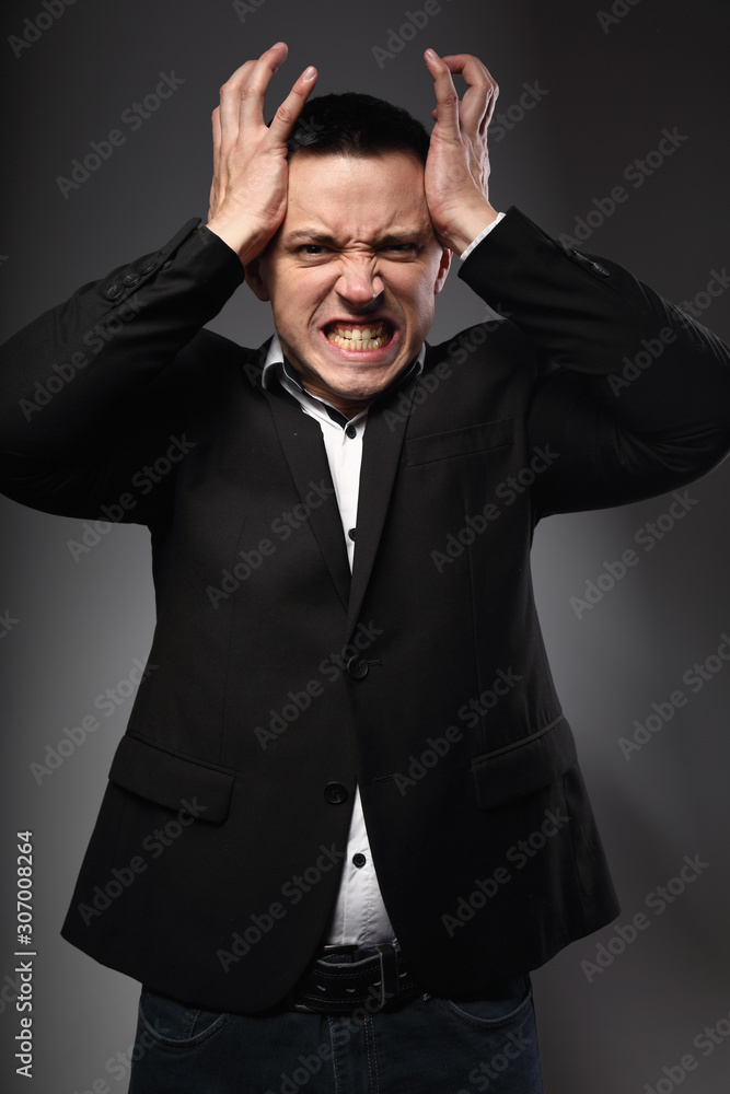 Angry business man in suit holding the head the hands on grey background. Closeup Angry business man in suit holding the head the hands on grey background. Closeup