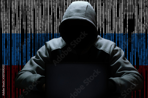 A Russian hacker is sitting in the dark in a hood in front of a computer, against a background of a binary code, the color of the Russian tricolor. Cybercrime