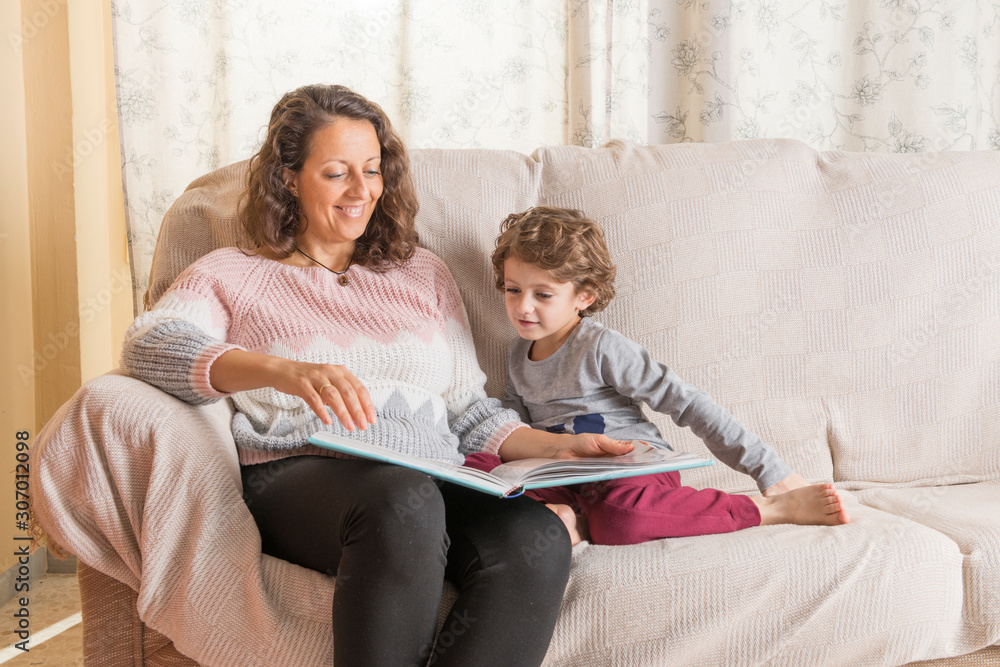 Child and a woman sitting on sofa reading a book.