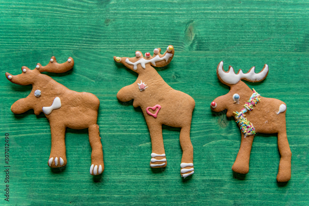 Festive, decorated gingerbread raindeer cookies on green wooden background. Christmas decorated, greeting cards concept 