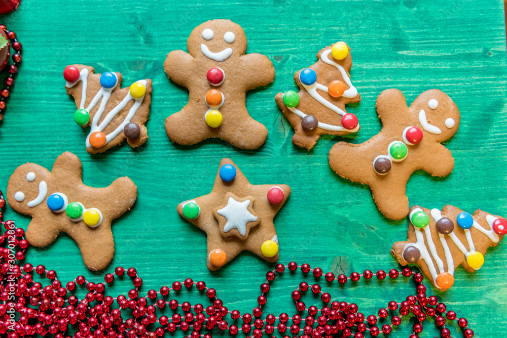 Obraz premium Colorful, decorated, gingerbread cookies, Christmas edition with red pearls, festive, on green wooden background 