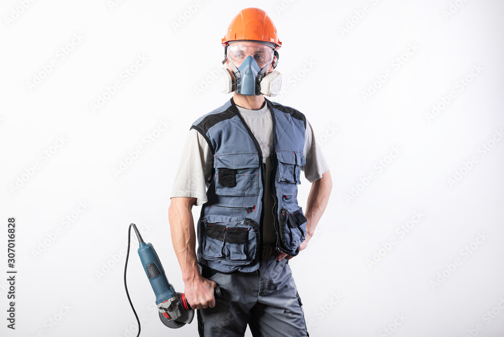 Builder in a helmet and a respirator, with an angle grinder in his hands. Builder in a helmet and a respirator, with an angle grinder in his hands.