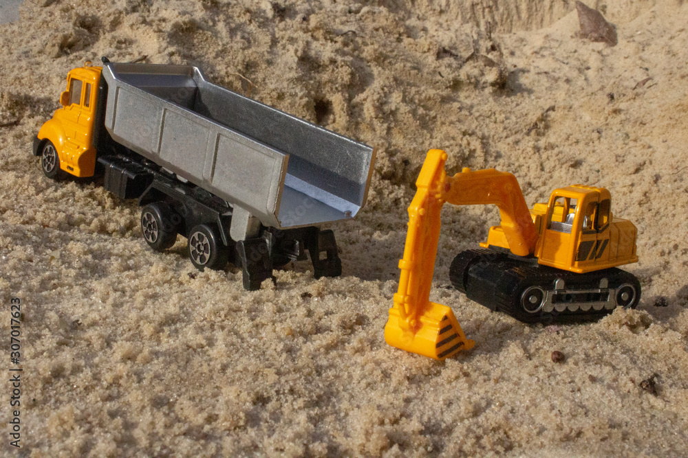 Toy excavator and yellow dump truck in the sand