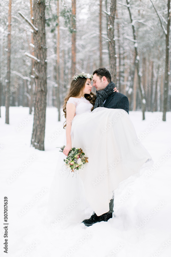 Winter wedding couple, bride and groom at their winter wedding day. Handsome groom holds her bride on hands Winter wedding couple, bride and groom at their winter wedding day. Handsome groom holds her bride on hands