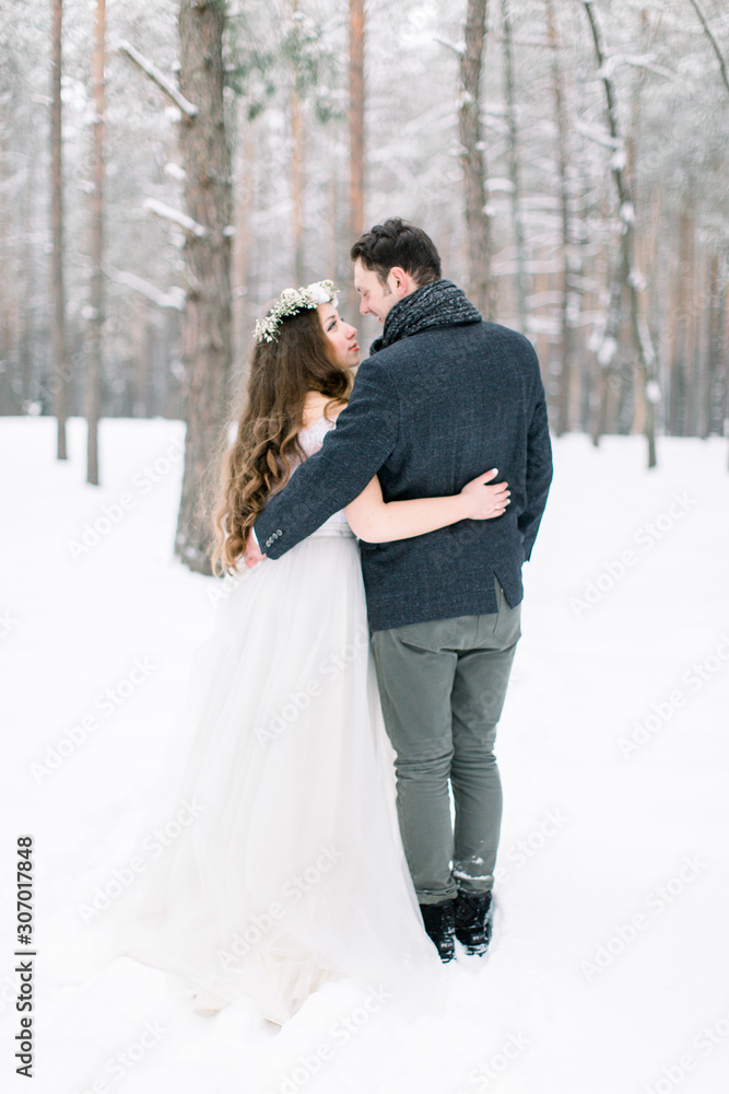 winter wedding in the forest, bride and groom embracing, standing and looking each other winter wedding in the forest, bride and groom embracing, standing and looking each other