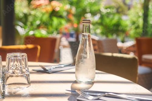 On a sunny day at small restaurant cold bottle of mineral water is standing on the table.