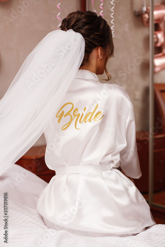 close up portrait a stylish bride in a robe with long veil with the inscription "the bride". brides morning in the hotel room. wedding morning.
