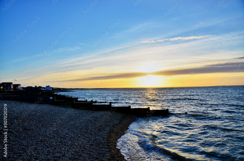 An evening view of a beautiful stony beach with the sea at a low tide and the sun setting on the horizon.