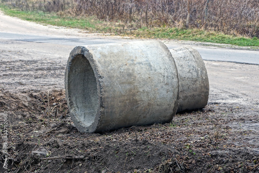 two gray concrete rings lie on the ground by the road two gray concrete rings lie on the ground by the road