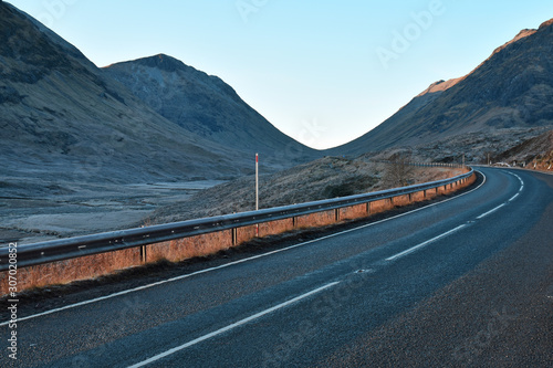 The A82 road as it winds through Glencoe in the Scottish Highlands. No visible vehicles or people. This is the main arterial route from Glasgow to Inverness via Fort William.