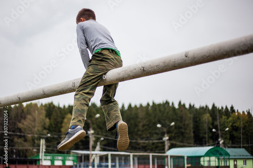 The child is sitting on the pipe. The boy climbed the gate photo