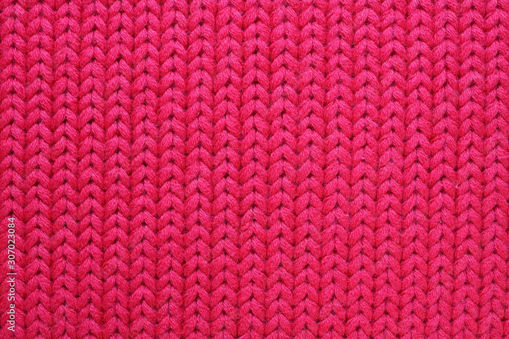 Red knitted texture closeup. Abstract woolen fabric background. Patterns of thick woven threads. Winter warm textile macro.