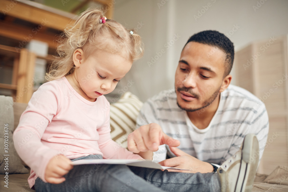 Portrait of young stay at home dad reading books with cute little daughter while enjoying tine together in home interior Portrait of young stay at home dad reading books with cute little daughter while enjoying tine together in home interior