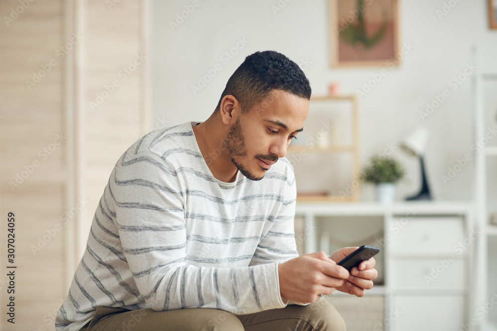 Side view portrait of modern mixed-race man using smartphone in home in home interior, copy space Side view portrait of modern mixed-race man using smartphone in home in home interior, copy space