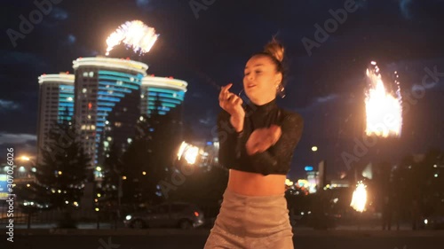 Performance or show with fire outdoor. Adult girl moves with flaming torches with group of fireshow artists. Concept of modern arts and culture. Slow motion, city landscape. photo