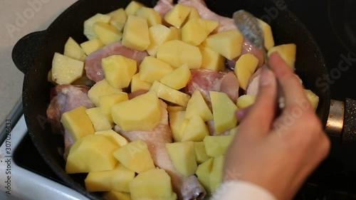 The process of cooking chicken with potatoes in a pan on the stove