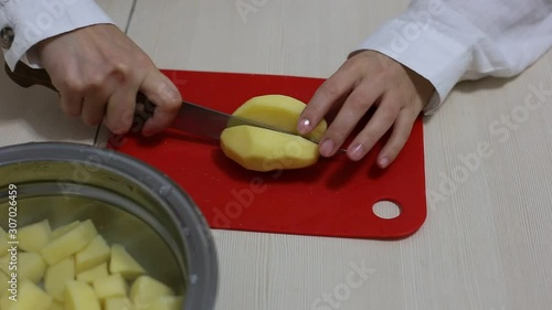 Hands cut potatoes on a red board on the table. Cooking process.