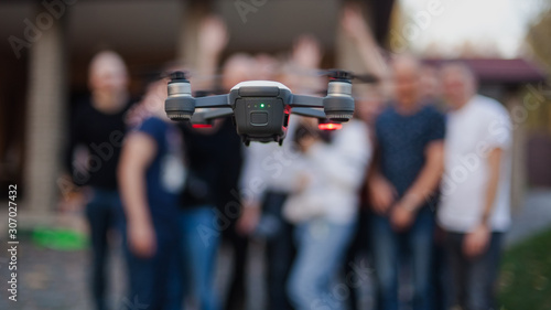 Flying drone, against the background of the company of young people. Unmanned aerial vehicles. Photos and videos from the drone. © Igor Savenchuk