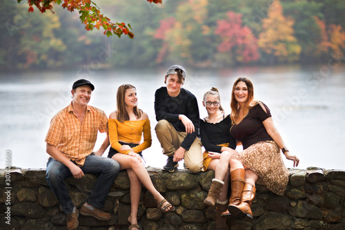 white Caucasian family sitting on a rocky wall, with the view on lake on fall. teenagers and parents. 