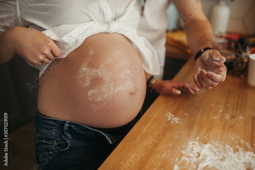 large naked pregnant belly with a handprint in flour, against a background of wooden kitchen stained with flour, a pregnant woman without a face bakes food