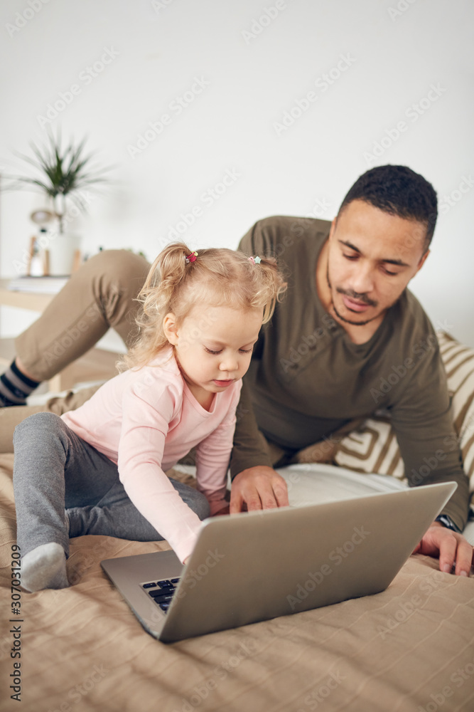 Portrait of little girl playing with father using laptop in cozy bedroom interior Portrait of little girl playing with father using laptop in cozy bedroom interior