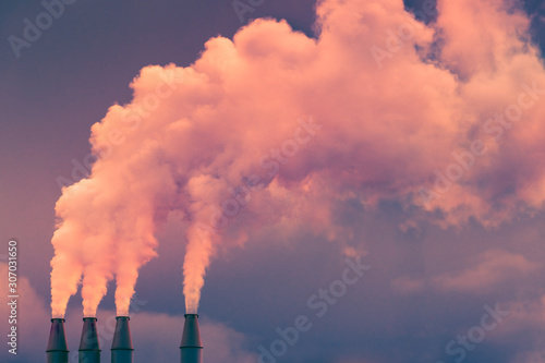 Smoke and steam rising into the air from power plant stacks; dark clouds background; concept for environmental pollution and climate change photo