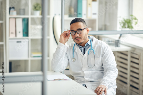 Portrait of African-American doctor looking at camera screen while sitting at desk in modern clinic, copy space