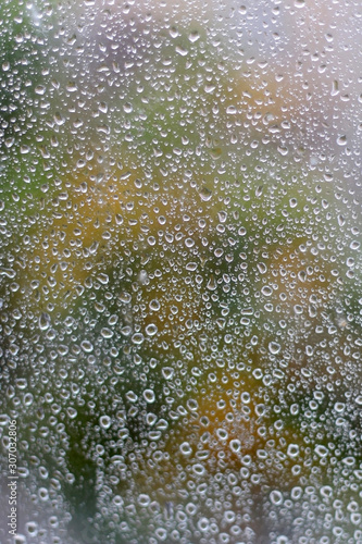 Rain drops on a window with garden view. Close-up, selective focus.