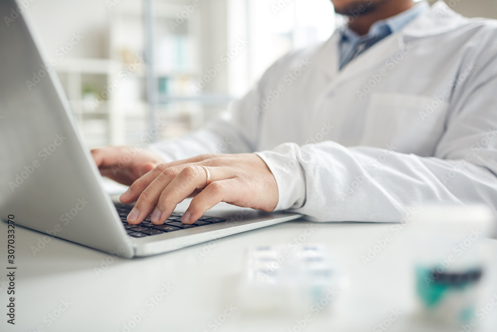 Close up of unrecognizable doctor using laptop at workplace in clinic, copy space Close up of unrecognizable doctor using laptop at workplace in clinic, copy space
